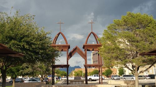 Low angle view of church gate amidst trees against cloudy sky during sunny day