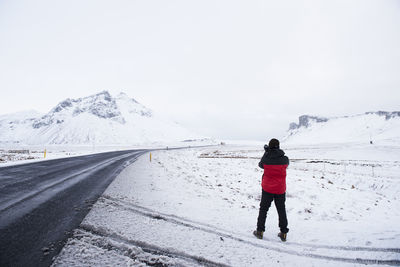 Rear view of man standing on snowcapped mountain road