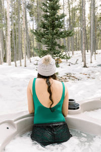 Woman from behind in a hot tub outdoors enjoying a view of trees during winter