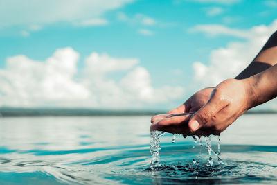 Person hand by sea against sky