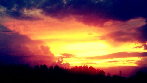 Silhouette trees against dramatic sky during sunset