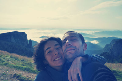 Portrait of loving couple standing on mountain against sky