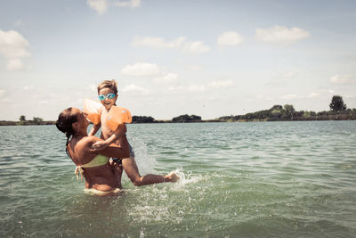 Woman playing with son in sea against sky