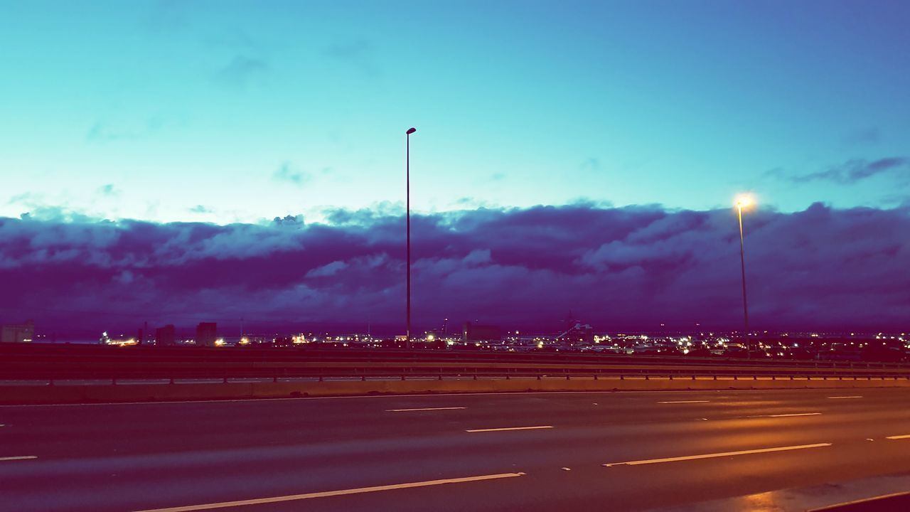 ROAD BY ILLUMINATED STREET LIGHTS AGAINST SKY AT NIGHT