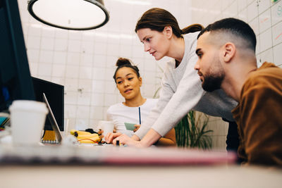 Young businesswoman using laptop while standing amidst colleagues at creative office