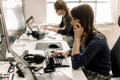 Female entrepreneur working on computer while talking on phone at workplace