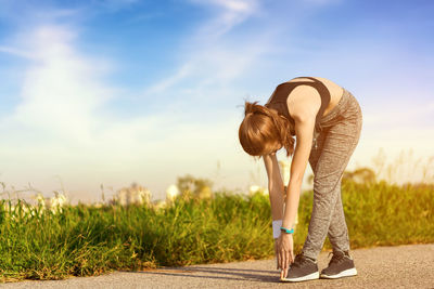 Young woman stretching while standing on road against sky