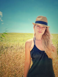 Portrait of young woman wearing hat standing on field against sky