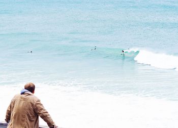 Rear view of men sitting on shore at beach