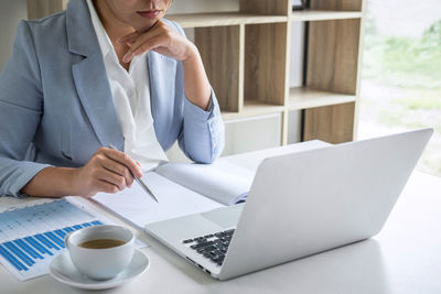 Midsection of businesswoman holding pen working in office