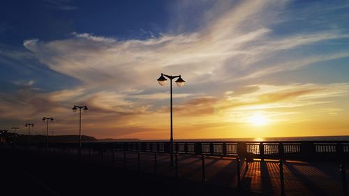 Silhouette street by sea against sky during sunset