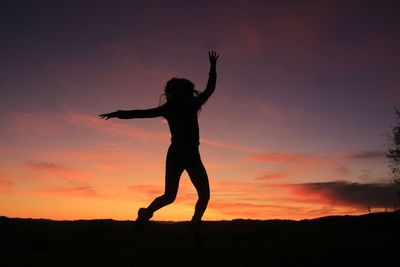 Silhouette woman with arms outstretched standing against sky during sunset