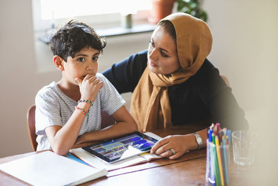 Mother looking at thoughtful son while studying at home