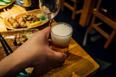 Cropped hand holding beer glass on restaurant table at night