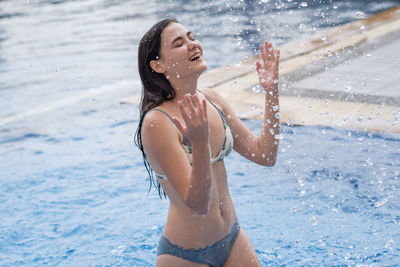 Cheerful woman splashing water while standing in swimming pool