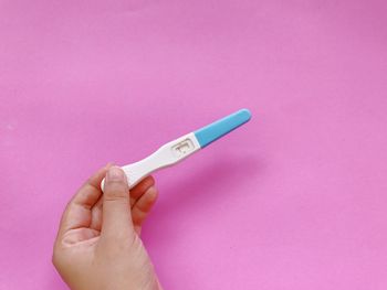 Close-up of hand holding paper over pink background