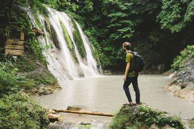 Side view of backpacker looking at waterfall while standing on rock in forest