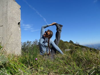 Woman stretching on grassy land against blue sky