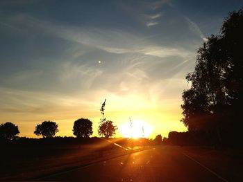 Road amidst silhouette trees against sky during sunset