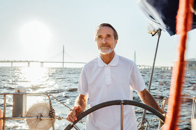 Senior man standing in sailboat against sky