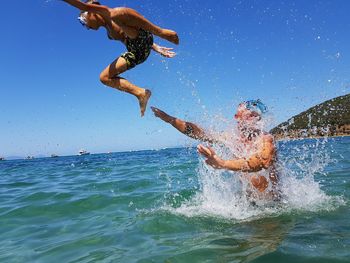 Playful father throwing son in sea against clear sky