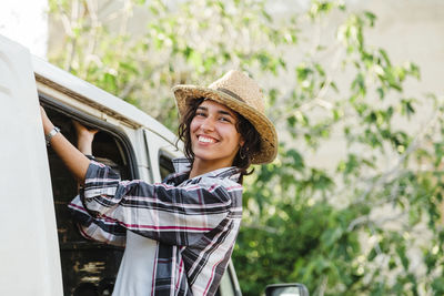 Portrait of smiling young woman wearing hat standing by car