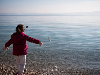 Rear view of girl throwing stones at beach