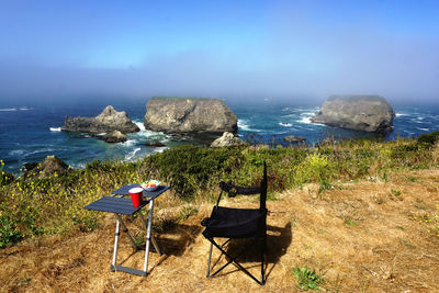 Chairs on rocks by sea against blue sky