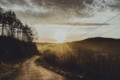 Road amidst trees against sky during sunset