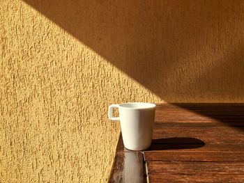 Minimalistic shot of a white cup sitting in the bright sunlight on a wooden table