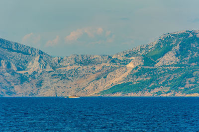 Scenic view of sea by mountain against sky