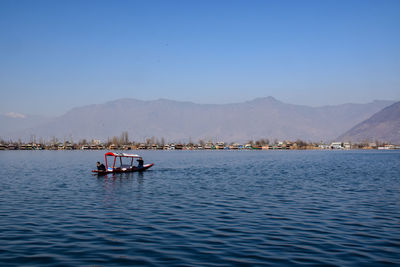 Boat in lake with mountains in backgrounds against clear blue sky