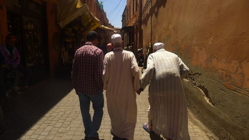 Rear view of men walking on footpath during sunny day