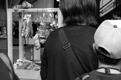 Rear view of woman standing by market stall selling sausages 