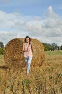 Full length of woman walking against by hay bale at field