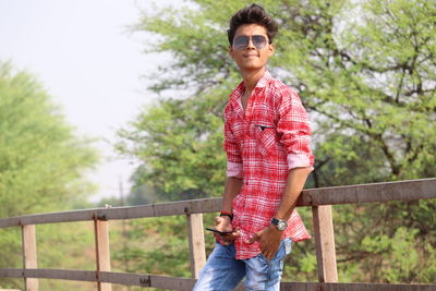Portrait of smiling man standing by railing against trees