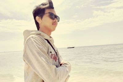 Young man wearing sunglasses on beach against sky