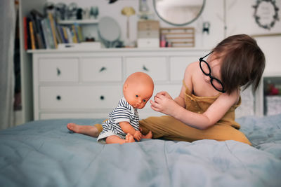 Cute child plays doctor in cozy interior. toddler child on bed with glasses glues patch to doll. 