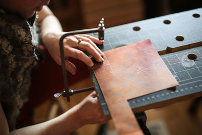 Master in the home workshop saws out a piece of copper metal with a jigsaw, concept creativity 