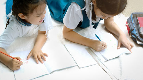 High angle view of girls studying while lying on floor at home