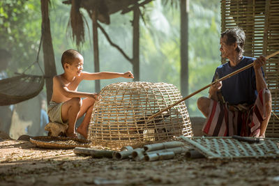 Boy and senior man removing chicken bird from wicker basket on field