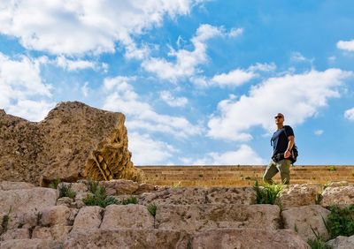 Low angle view of man standing on rock against sky