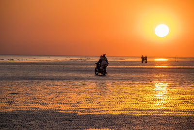 Silhouette man riding motorcycle on beach against sky during sunset
