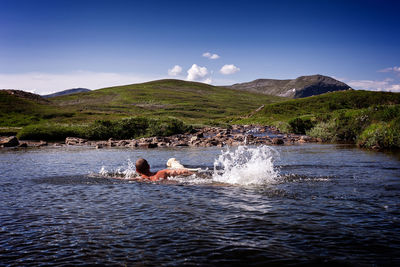 Man swimming with dog in lake against sky