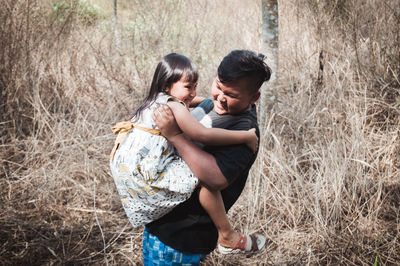 Side view of brother carrying cute sister while standing on grassy field