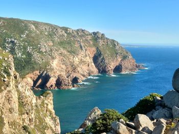 Scenic view of sea by cliff against clear blue sky