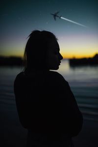 Silhouette woman looking at lake against sky during sunset