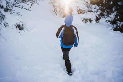 Rear view of man walking on snow covered land during winter