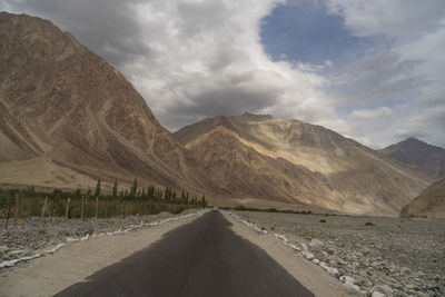 Empty road by mountains against sky