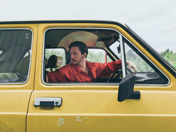 Man sitting in car against sky